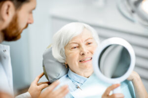 Elderly woman smiling at her reflection in a dental office mirror