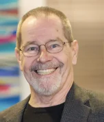 Professional headshot of a man with glasses and beard smiling in a dental office setting.