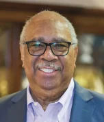 Professional headshot of a man with glasses wearing a dark blazer and light blue shirt.